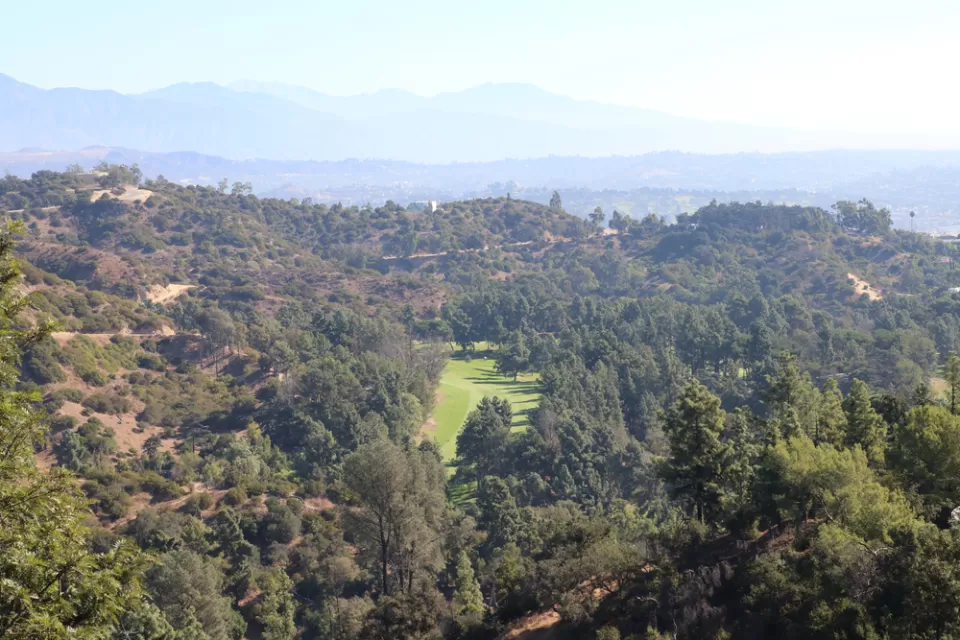 The fairway of a golf course is visible amidst the rolling hills of Griffith Park above Los Angeles.
